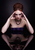 portrait of beautiful young woman sitting at dark reflecting table touching head temples with hands