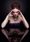 portrait of beautiful young woman sitting at dark reflecting table touching head temples with hands